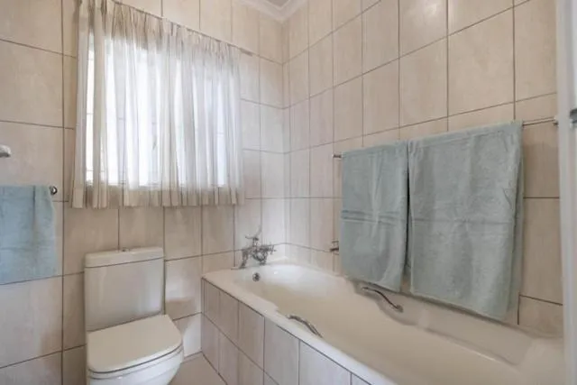 Bathroom with tiled walls, a bathtub, toilet and hanging towels near a curtained window