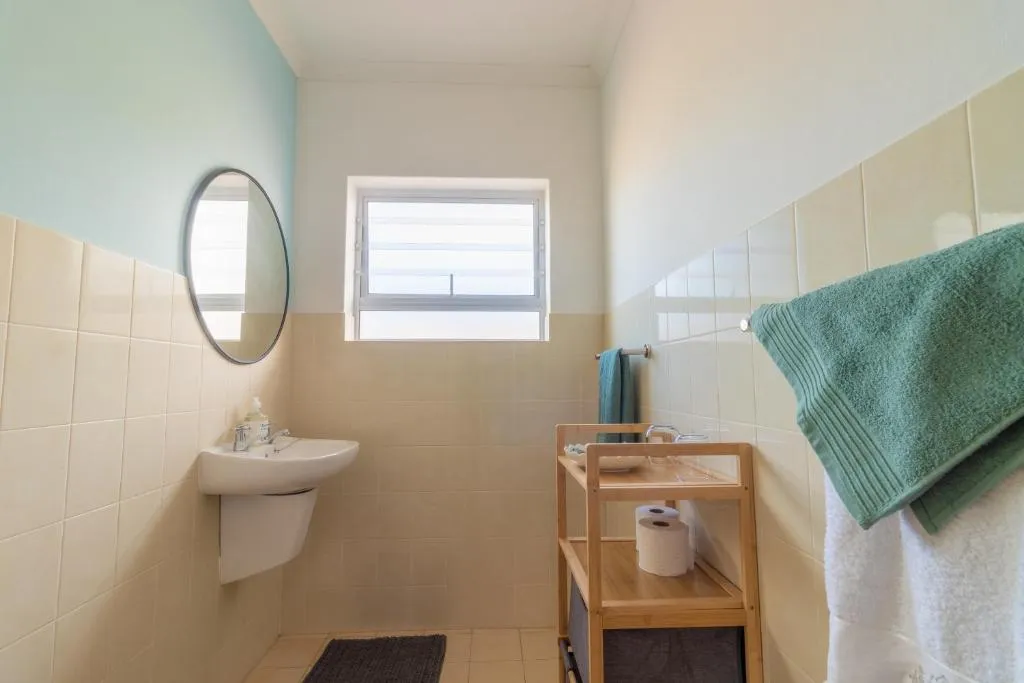 Bathroom with a wall-mounted basin, round mirror and a shelving unit for towels