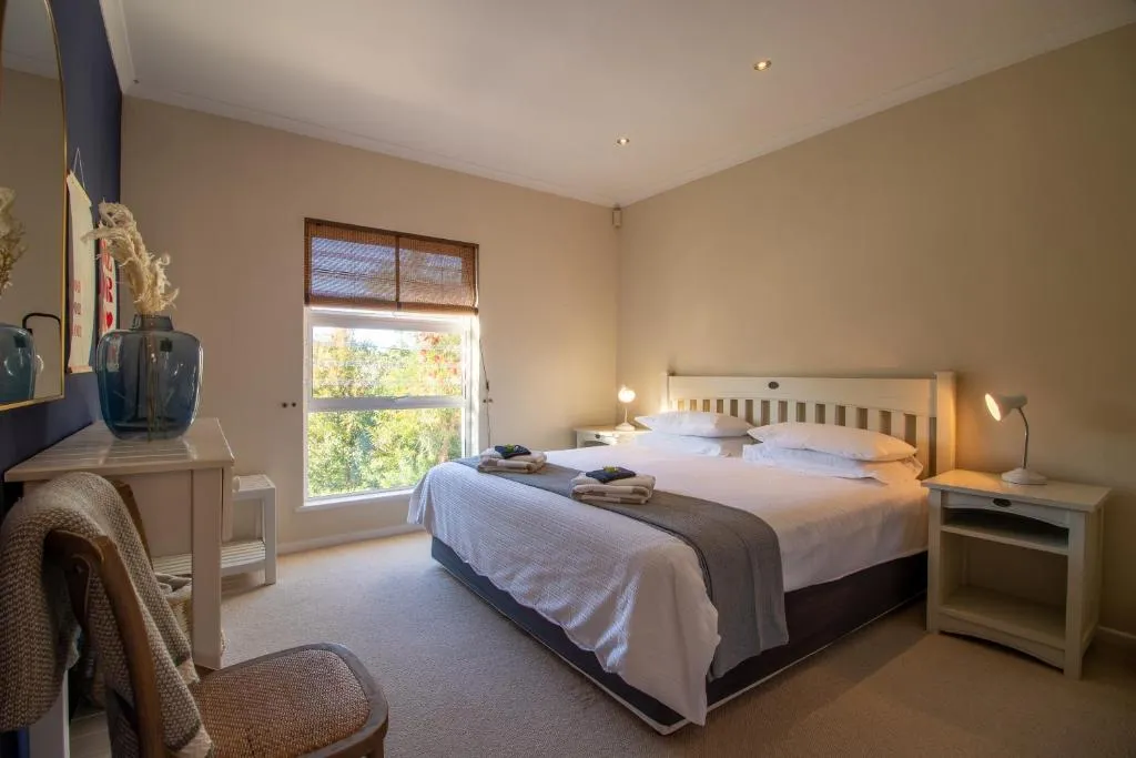 Bedroom with a queen bed, bedside lamps and a window looking onto leafy garden trees