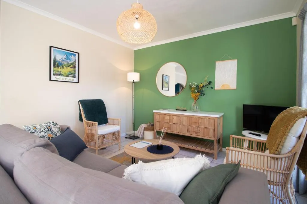 Living room with a green accent wall, rattan armchairs and a grey sofa around a coffee table