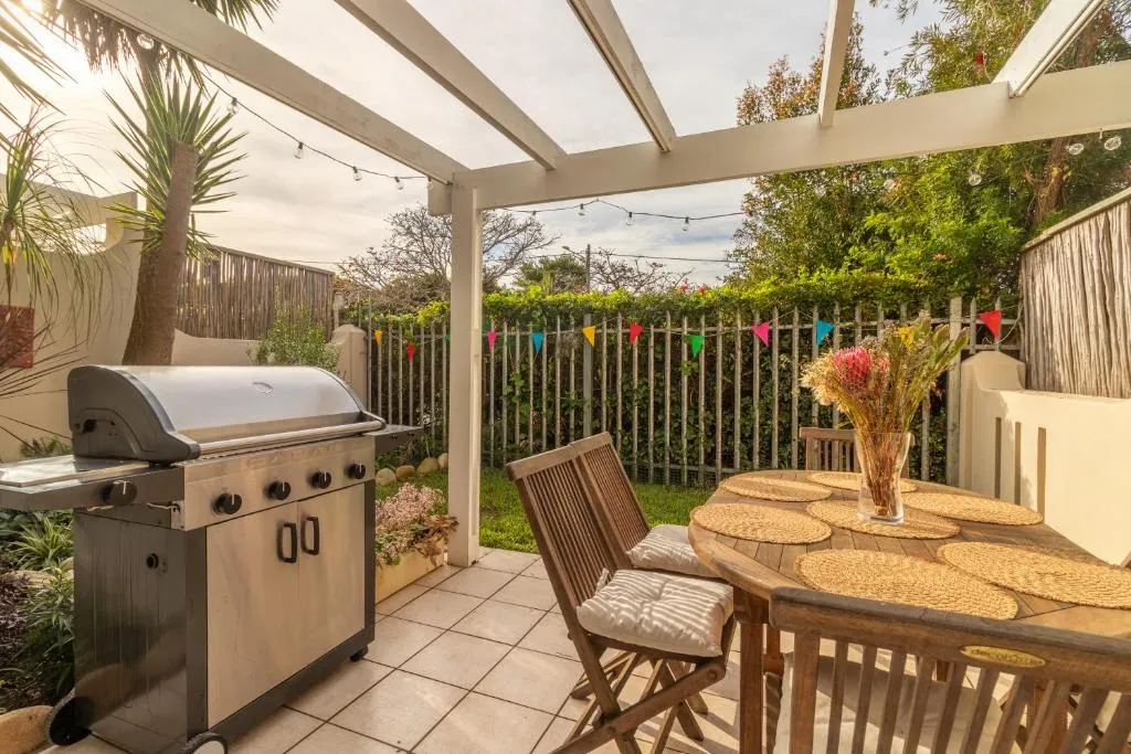 Covered patio with a gas braai, outdoor dining table set for six and bunting strung along the fence
