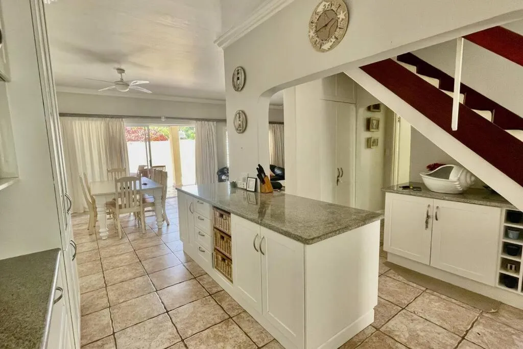 Open-plan kitchen with a granite island, staircase and a dining table visible beyond