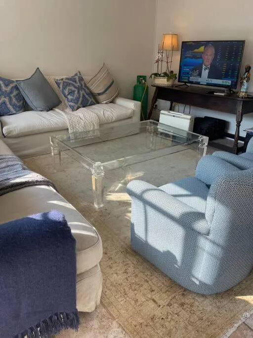 Second lounge with a pale sofa, blue armchair, glass coffee table and wall-mounted TV