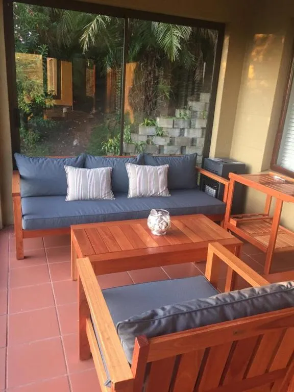 Covered outdoor lounge with timber sofas and cushions beside a stone garden wall
