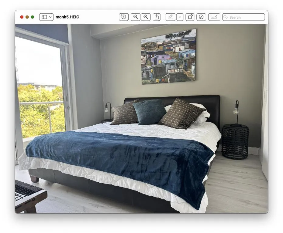 Bedroom with a king bed, local artwork above the headboard and a glass door onto a balcony