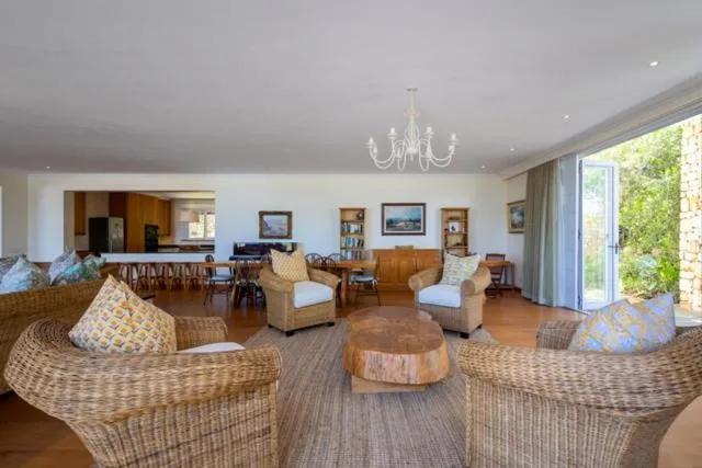 Open-plan living and dining room with wicker armchairs, a chandelier and doors onto the garden