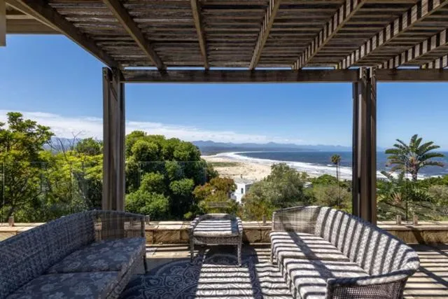 Covered pergola deck with wicker sofas overlooking a long white beach and the bay beyond