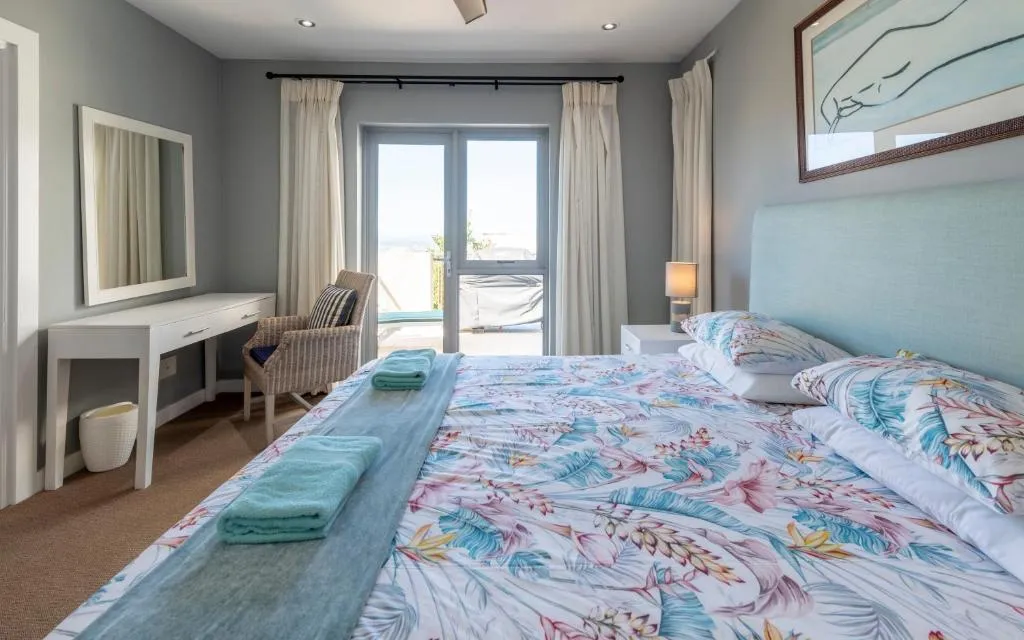 Same bedroom viewed toward the dressing table, wicker chair and mirror, with balcony doors beyond
