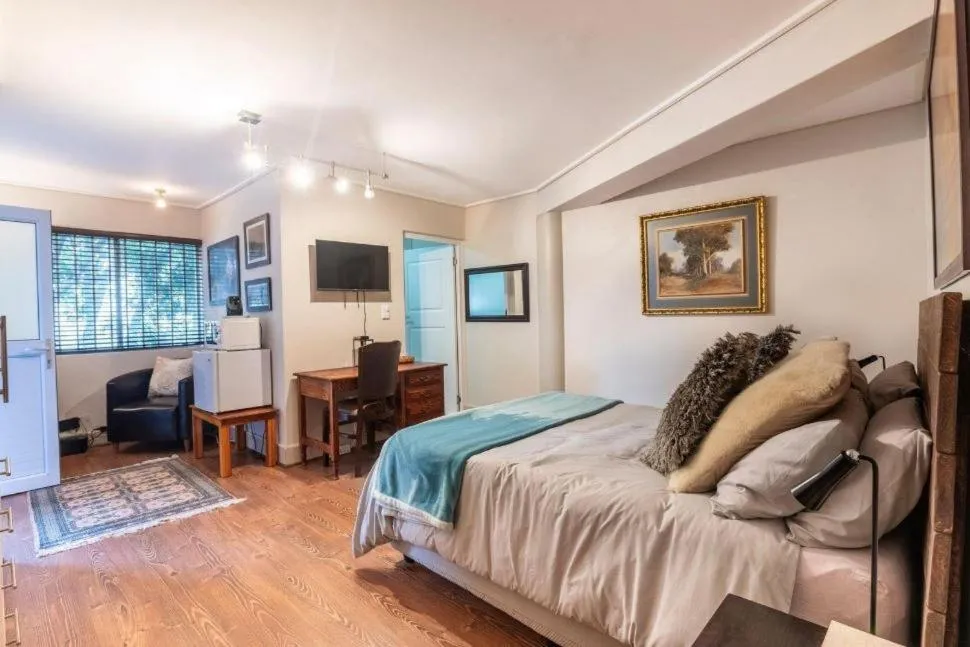 Bedroom with wood floors, wall-mounted TV, work desk and a framed painting above the bed