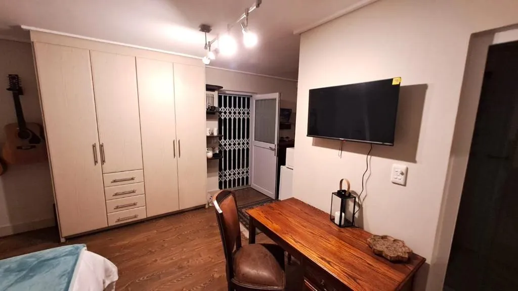 Bedroom with built-in wardrobe, work desk, wall-mounted TV and an acoustic guitar on display