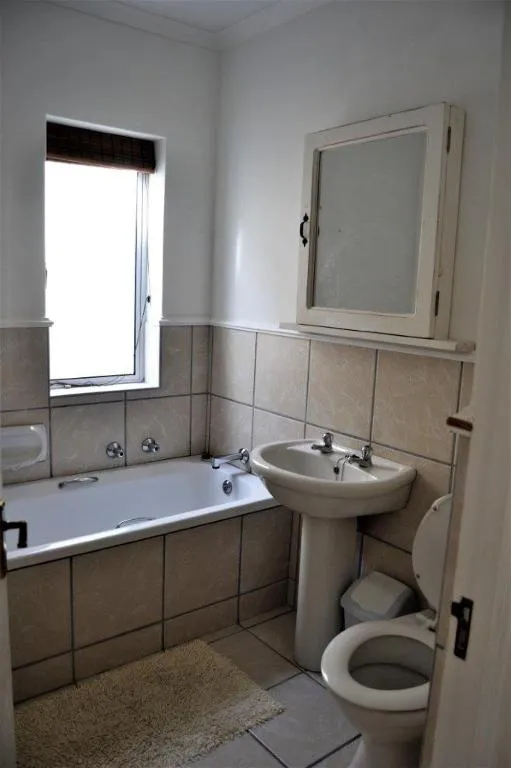 Compact bathroom with a built-in bath, pedestal basin and toilet under a window