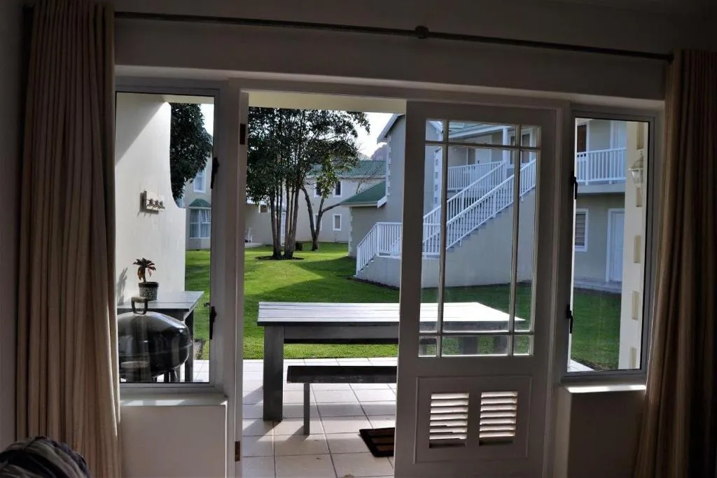 Patio doors open onto a courtyard with a kettle braai, bench table and lawn beyond