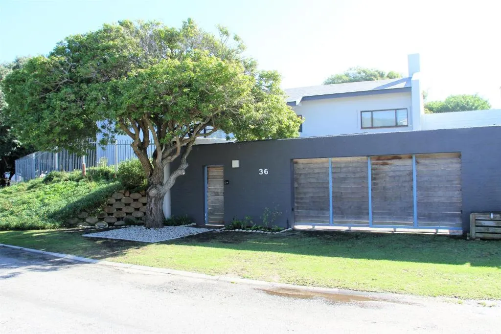 House exterior numbered 36, with a grey boundary wall, garage door, and manicured lawn