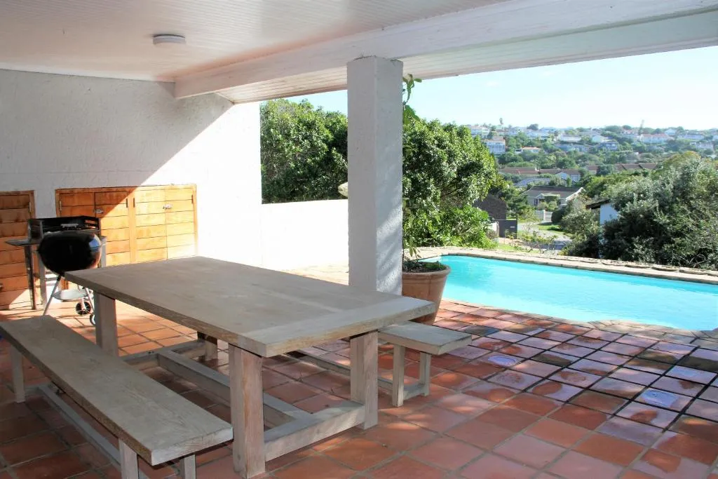 Covered patio with a braai and dining setup overlooking the pool and hillside suburb