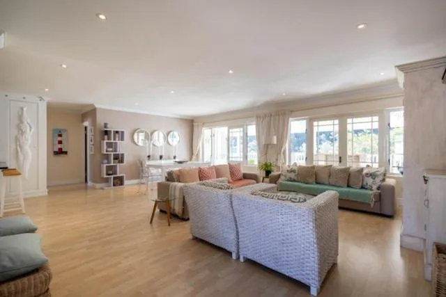 Living room with wicker armchairs and sofas facing French doors onto a wooded hillside garden