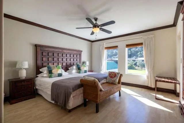 Bedroom with dark wood headboard, ceiling fan and twin windows looking onto trees
