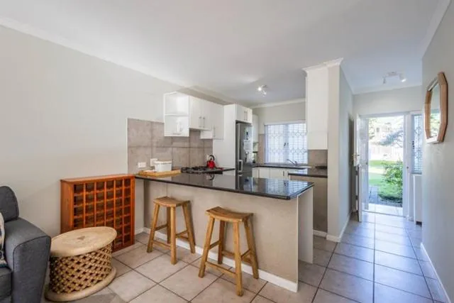 Galley kitchen with black countertop breakfast bar, two wooden stools and gas hob
