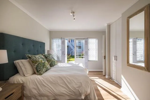 Main bedroom with teal upholstered headboard and folding doors onto a small garden-facing balcony
