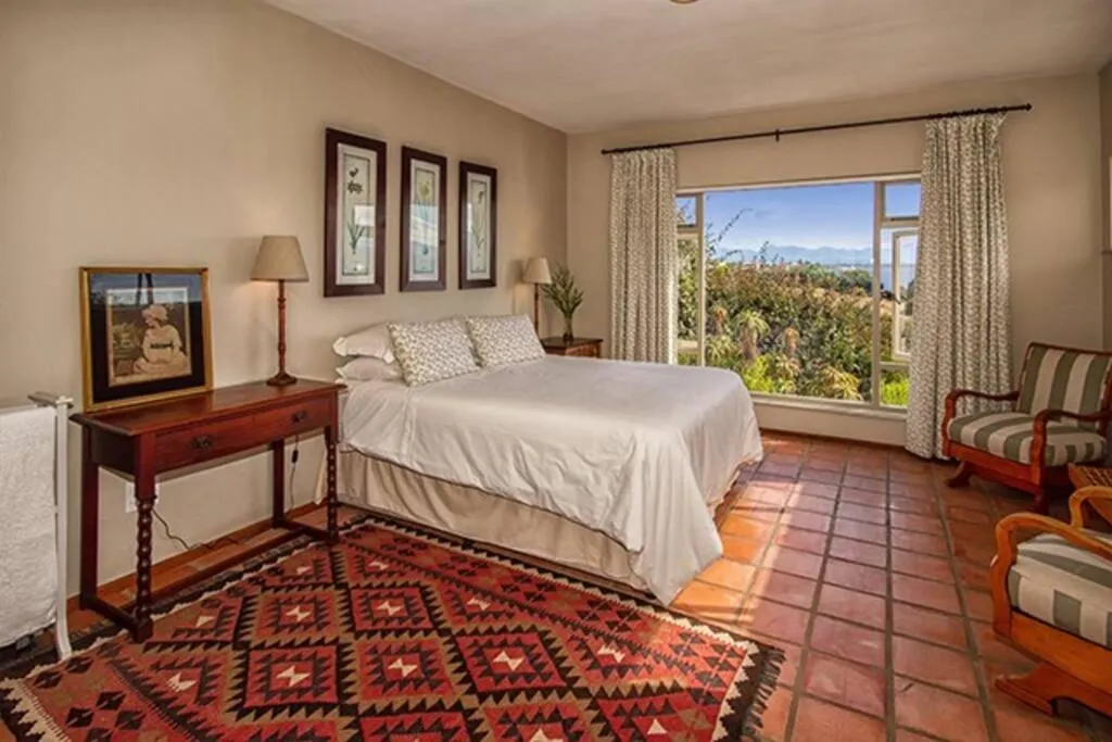 Bedroom with a kilim rug and a large window looking over the garden to the lagoon and mountains beyond