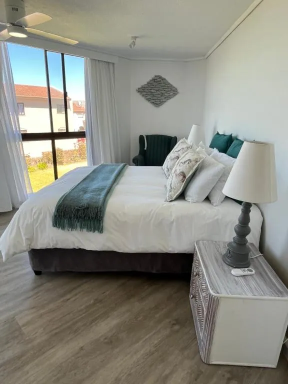 Bedroom with teal and white linens, a green armchair and a ceiling fan