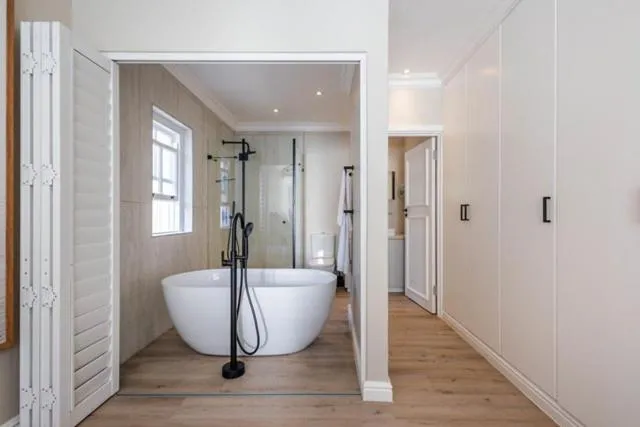 Freestanding bathtub beside a glass shower and a walk-in wardrobe with built-in cupboards