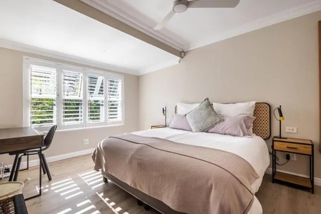 Bedroom with plantation shutters, a wood desk, and light oak flooring