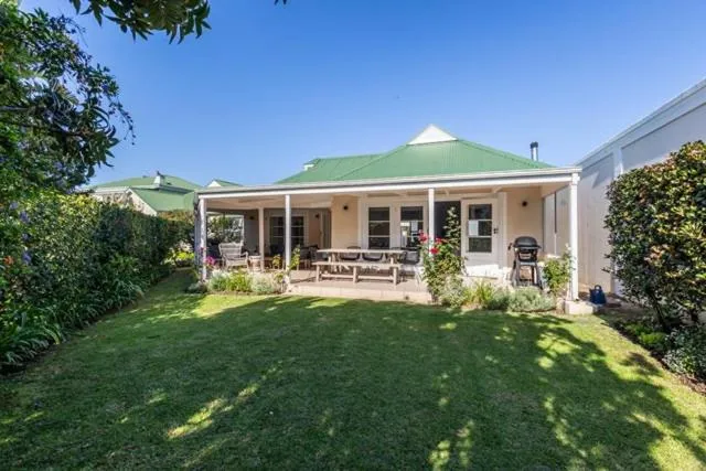 Cape-style cottage with a green pitched roof, covered veranda, garden lawn, and a built-in braai