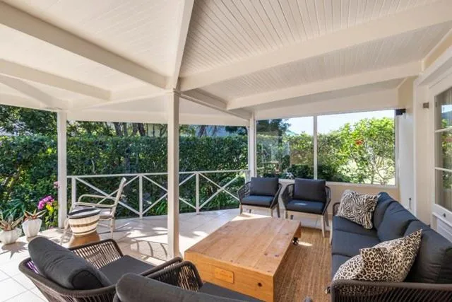 Screened veranda with rattan-style lounge seating and a coffee table, facing the hedge-lined garden