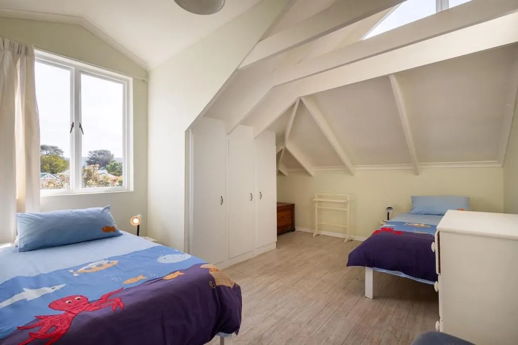 Twin bedroom with nautical-themed bedding, sloped ceiling and a window looking over the treetops