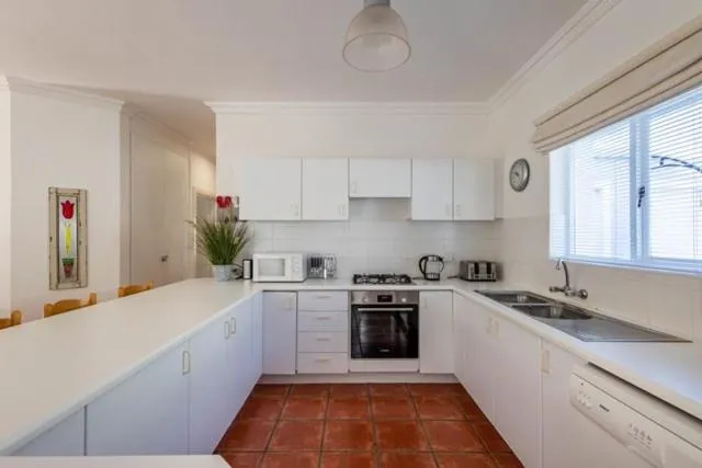 White fitted kitchen with a gas stove, dishwasher, and terracotta-tiled floor