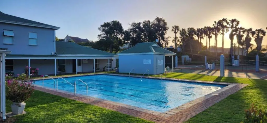 Shared estate swimming pool and clubhouse with a tennis court and palm trees beyond