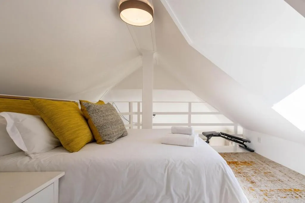 Loft bedroom under the eaves with white linens, mustard cushions and folded towels