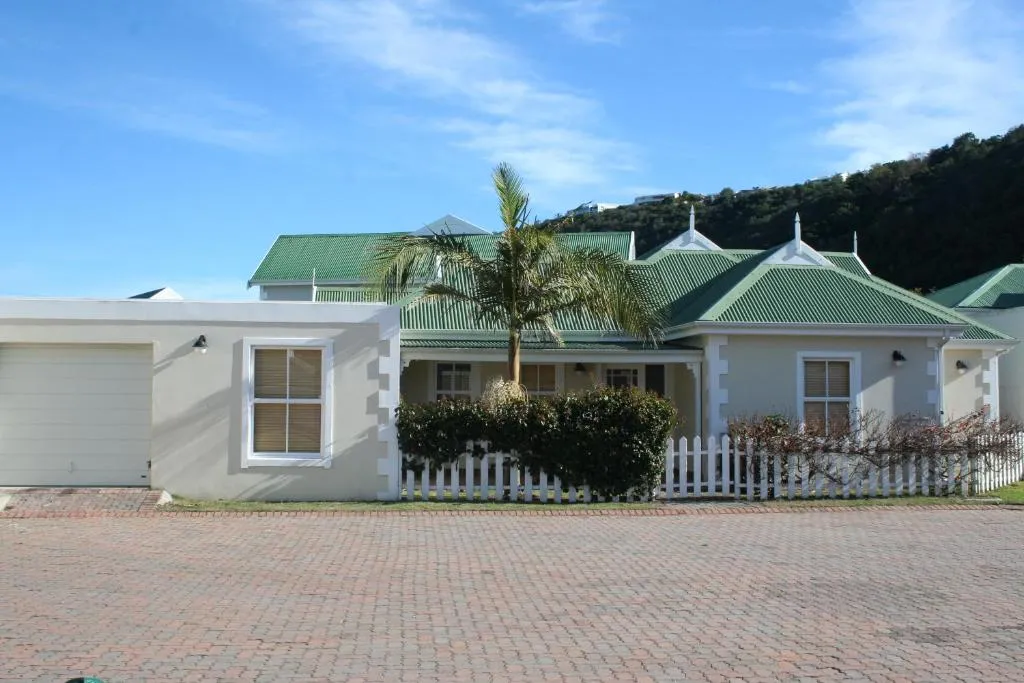 Cape Dutch-style single-storey home with green corrugated roof, palm tree and white picket fence at the entrance