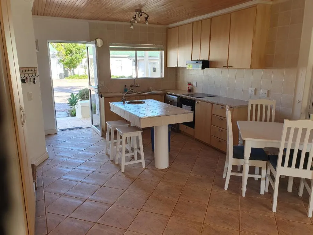 Kitchen with tiled central table, wooden cabinetry and door open to the garden path
