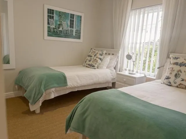 Twin beds with sage green throws and a coastal photograph in a bright bedroom