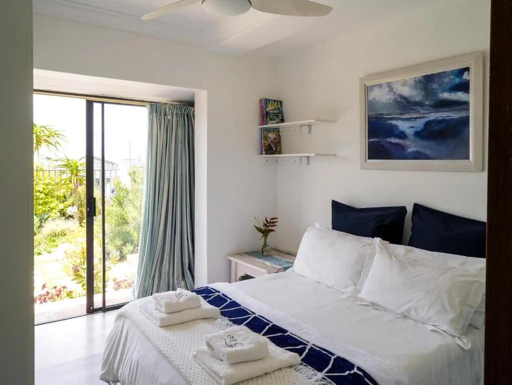 Bedroom with a ceiling fan, seascape painting and sliding doors opening onto the garden