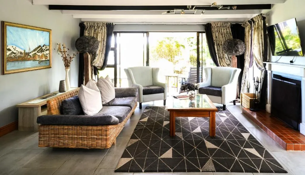 Living room with a wicker sofa, armchairs and tiled fireplace, glass doors opening onto the garden