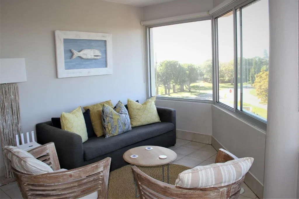 Bright sunroom lounge with a grey sofa and armchairs in a bay window overlooking a tree-lined street