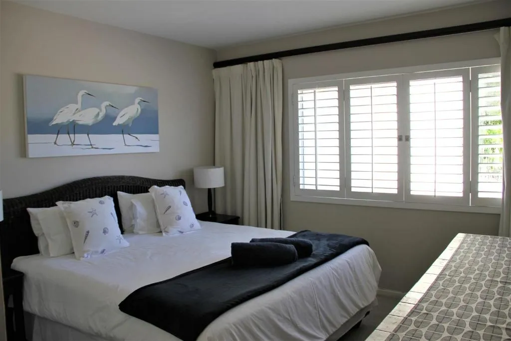 Bedroom with a dark wicker headboard, white linens and plantation shutters over the window