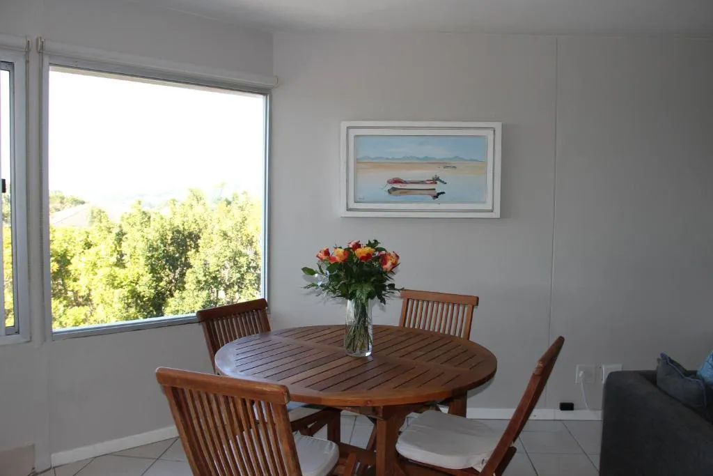 Round wooden dining table for four beside a window looking onto trees and garden greenery