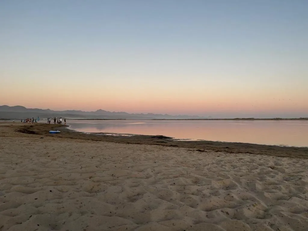 Lagoon and sandy beach at sunset with mountains silhouetted in the distance