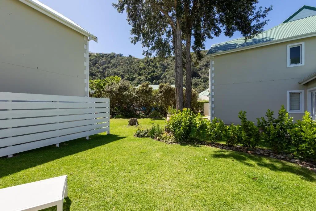 Back garden lawn bordered by a white fence, hedge and trees