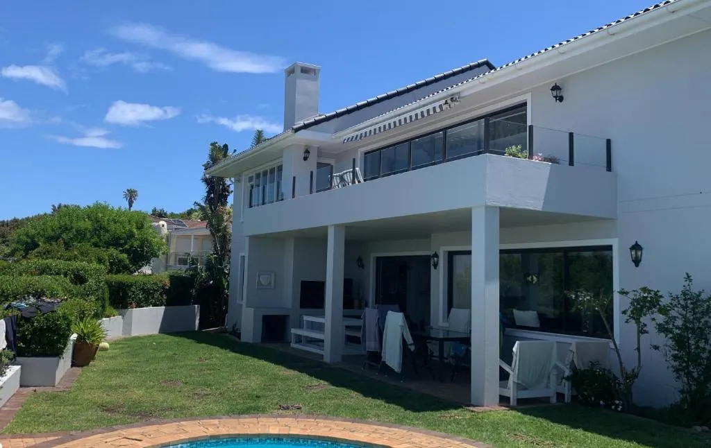 Double-storey house exterior with upper balcony and covered patio seating over the pool