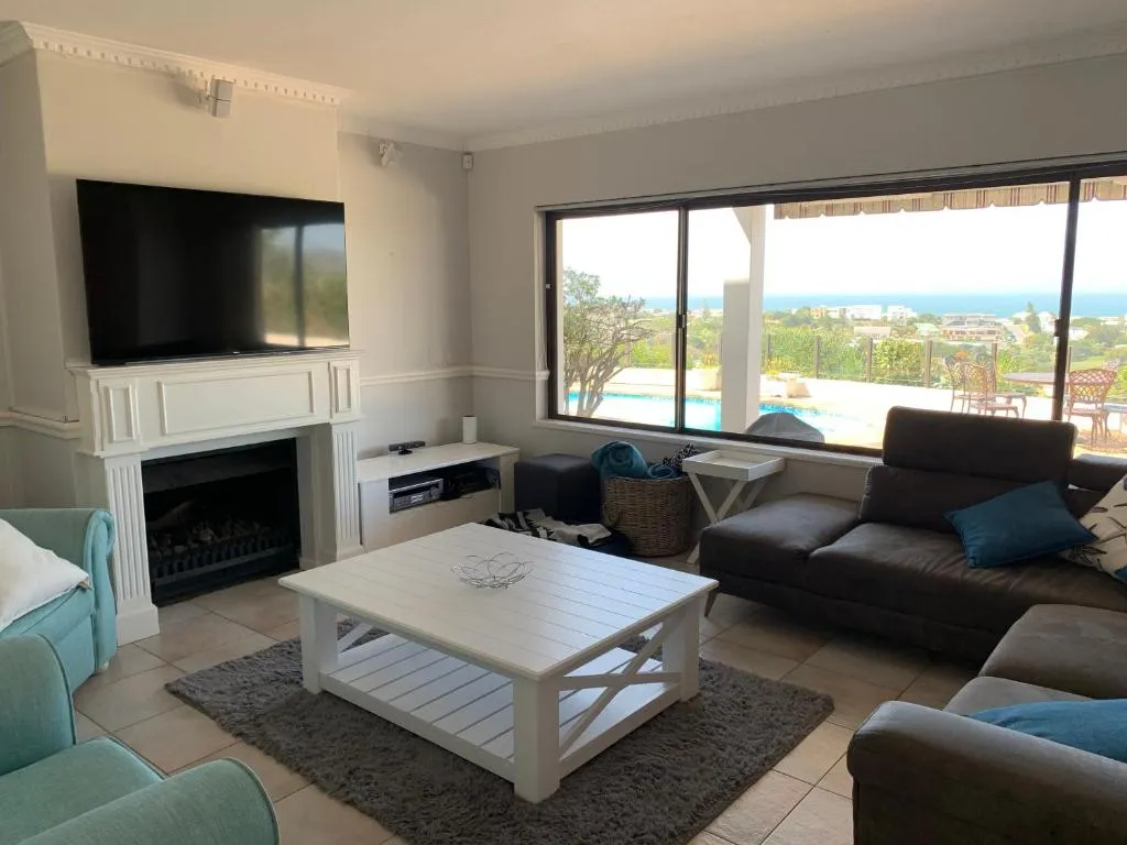 Living room with fireplace, TV, and sliding doors framing the pool and sea beyond