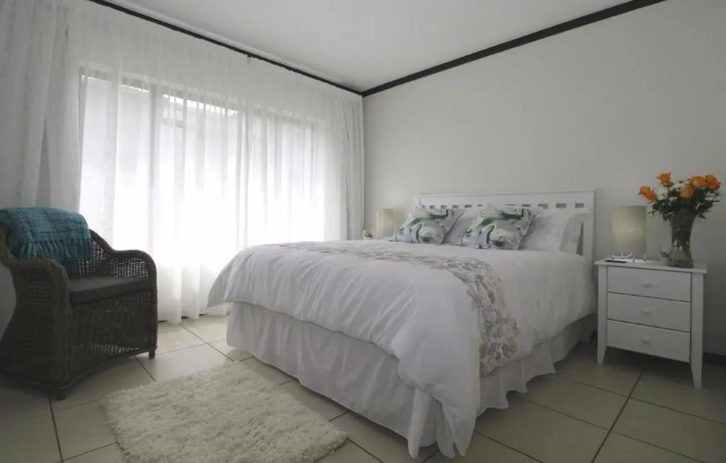 Bedroom with white bed linen, sheer curtains and a wicker armchair