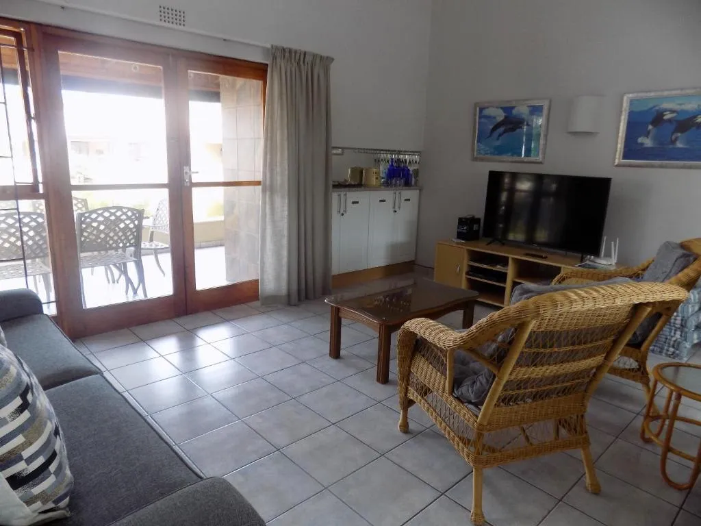 Living room with wicker armchairs, a wall-mounted TV and sliding doors onto a furnished balcony