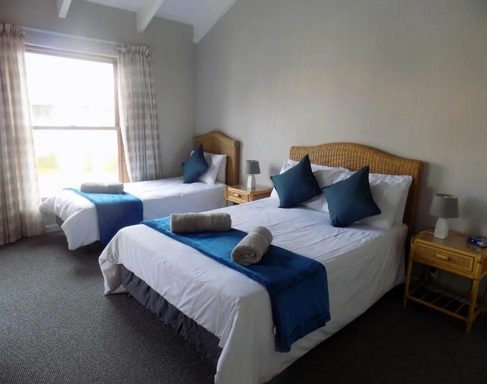 Twin bedroom with cane headboards, navy cushions and rolled towels on white linen