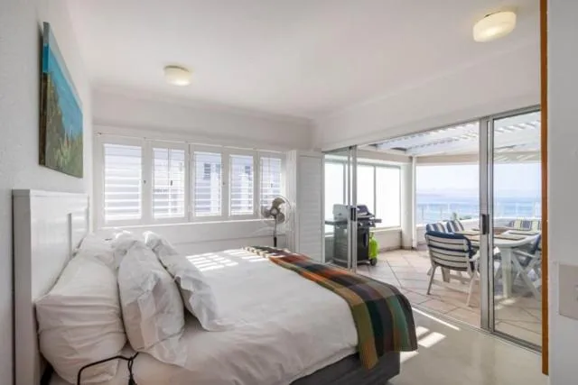 Bedroom with shutter windows and sliding doors opening onto a balcony with a braai and sea view