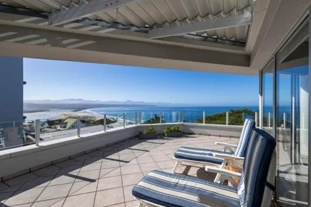 Covered terrace with striped lounge chairs under a pergola, overlooking the beach and ocean