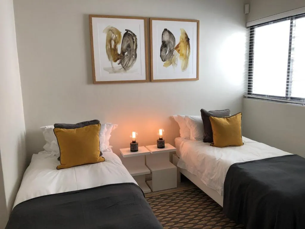 Twin bedroom with charcoal throws, mustard cushions and abstract wall art